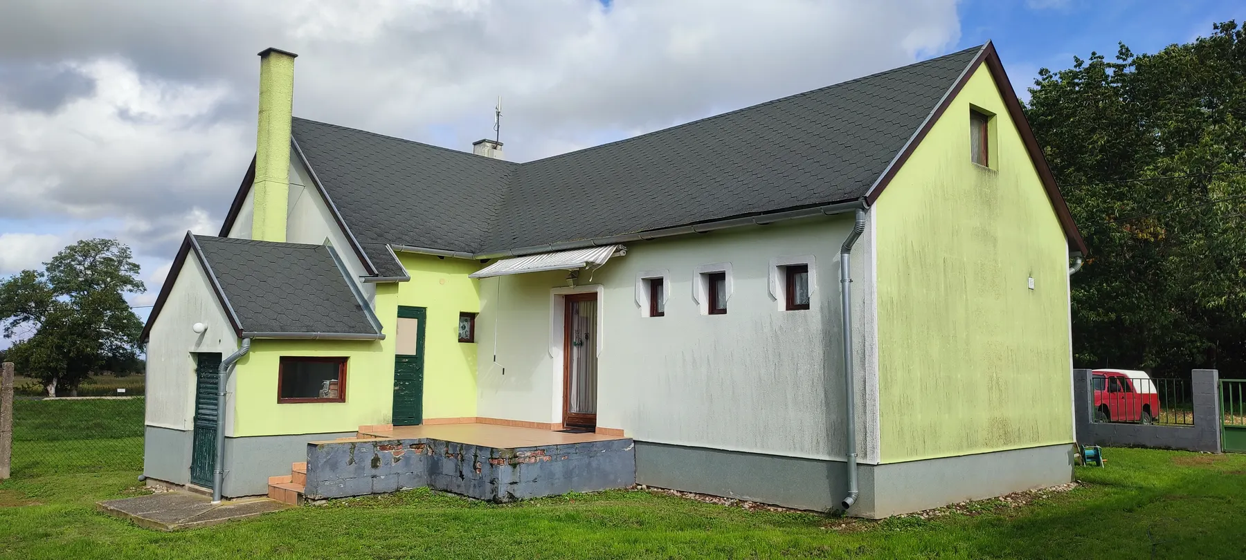 L alakú családi ház zöld, foltos homlokzattal, felújítás előtt